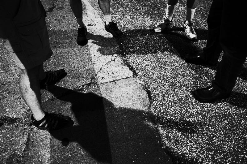 A group of men talk in a parking lot but only their footwear is shown