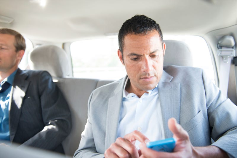 Business person in a car looking at their smartphone. They seem uneasy.