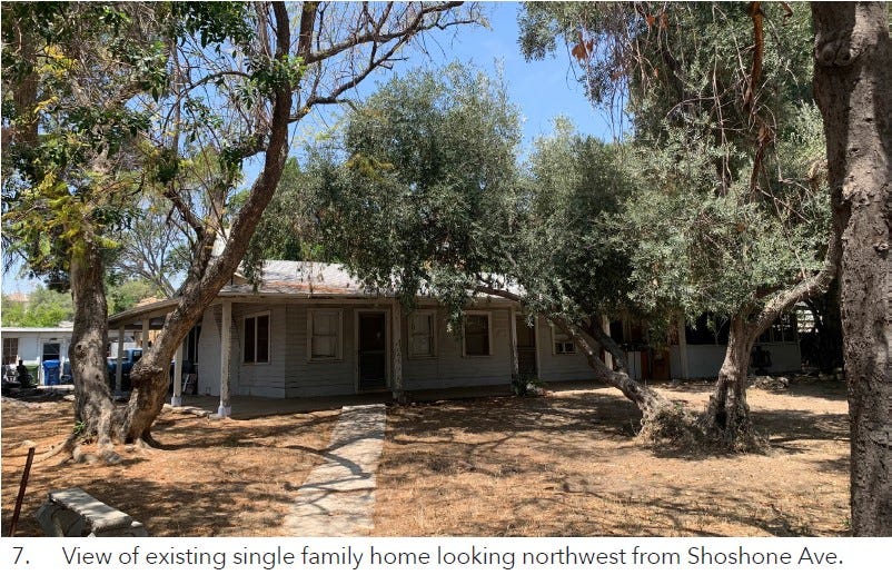 A home is viewed through trees. Caption states: “7. View of existing single family home looking northwest from Shoshone Ave.”