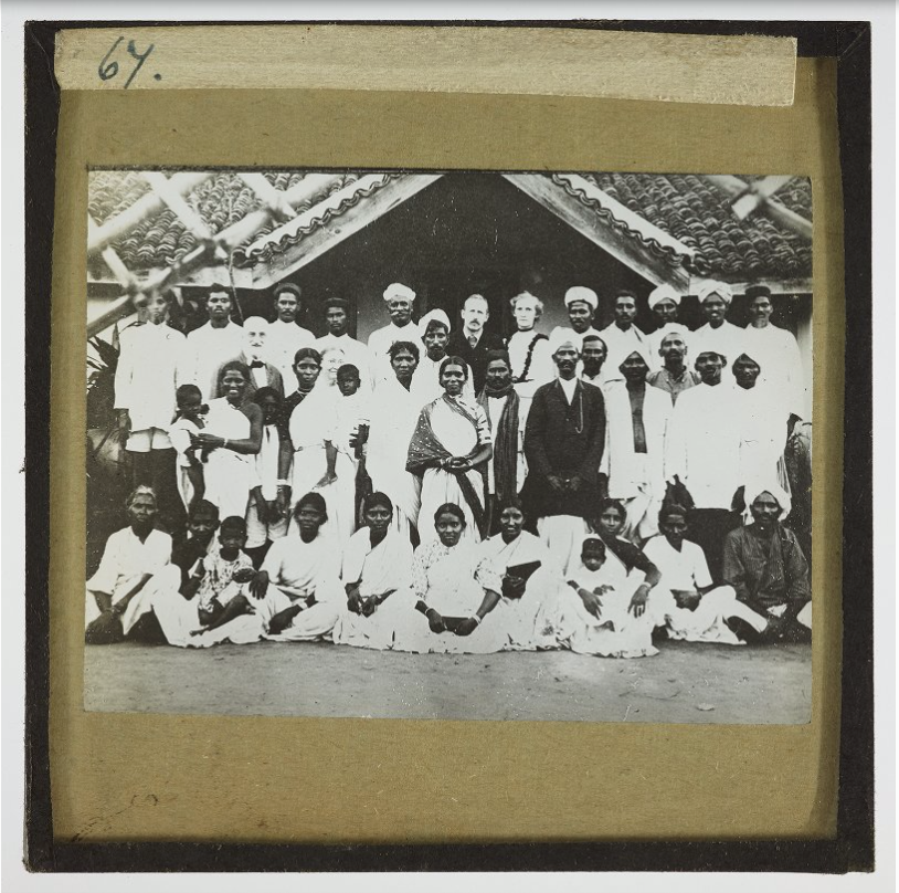 Black and white photograph of a white missionary couple (centre) surrounded by Indian men and women and children wearing white.