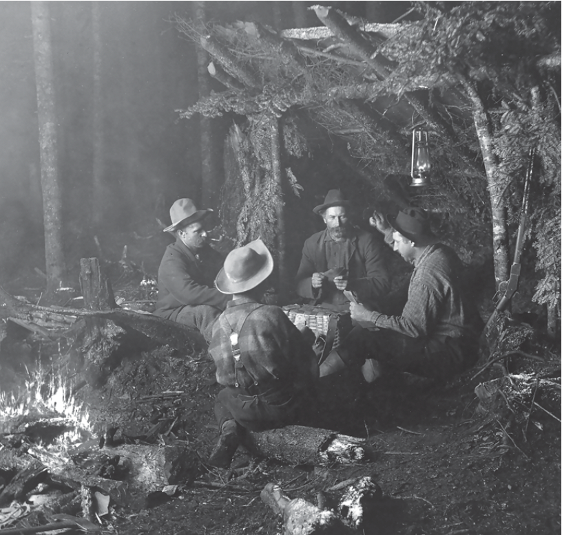 four men playing cards by a campfire in a lean-to