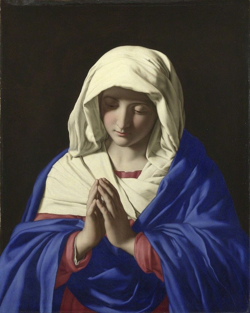Virgin Mary wears blue-colored robes with hands folded in prayer