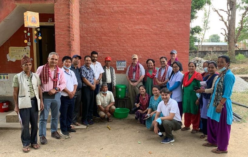 A group of men and women stand on either side of a bright green water dispenser in Nepal.