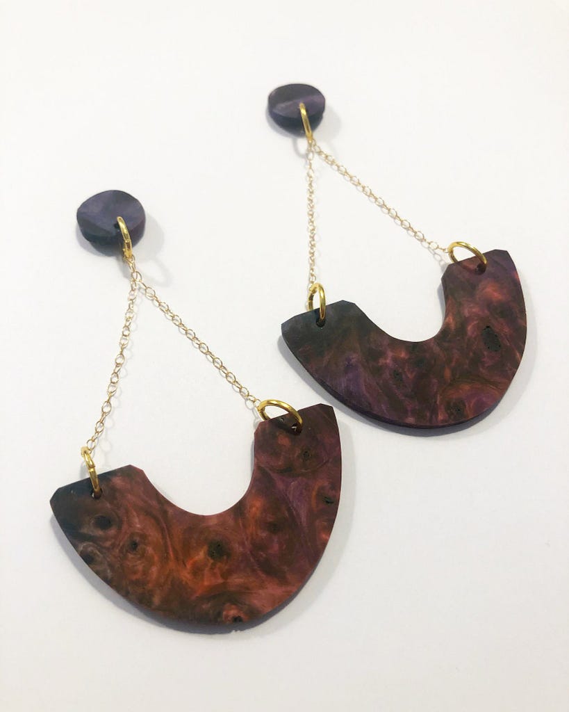 A pair of dangle earrings with round brown studs with 14K gold findings and chain connecting a larger brown wood burl pendant