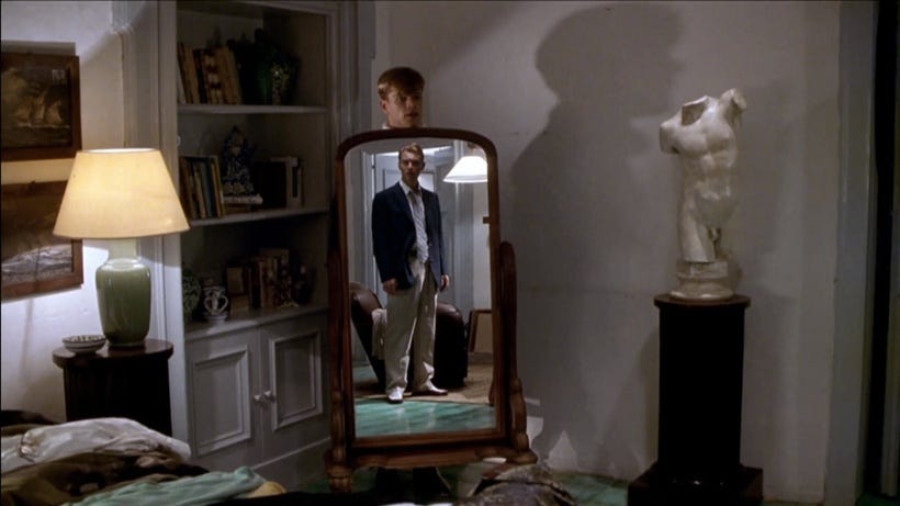 A shot from ‘The Talented Mr. Ripley’ showing Dickie looking in a mirror from which Tom’s head can be seen from behind. There is a headless bust of Michaelangelo’s David to the right of the mirror.
