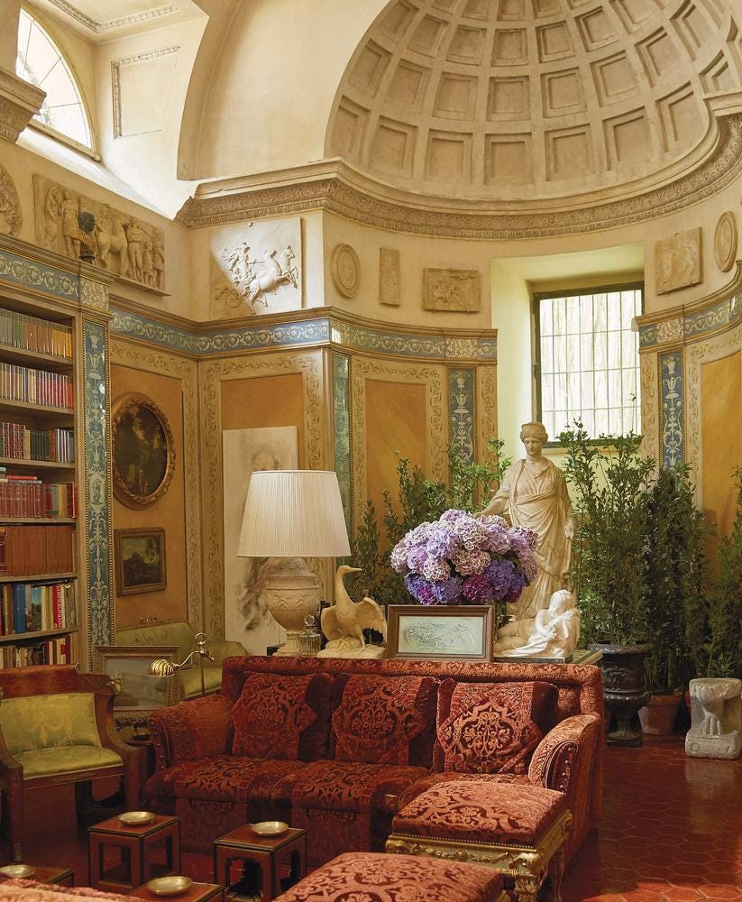 Baroque style room by Renzo Mongiardino, features a greek inspired sculpture, high ceilings, ambient lighting, plants and a bookshelf.