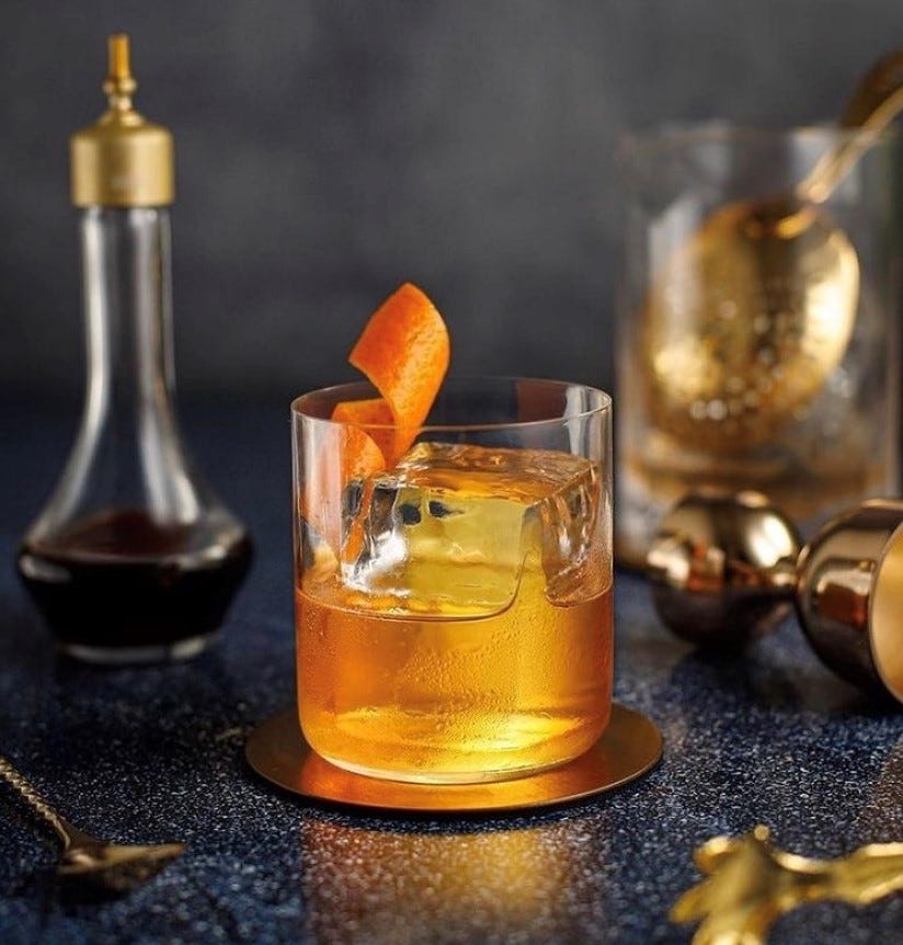 Old Fashioned Cocktail in a Modern Glass with a Large Ice Cube and Orange Twist