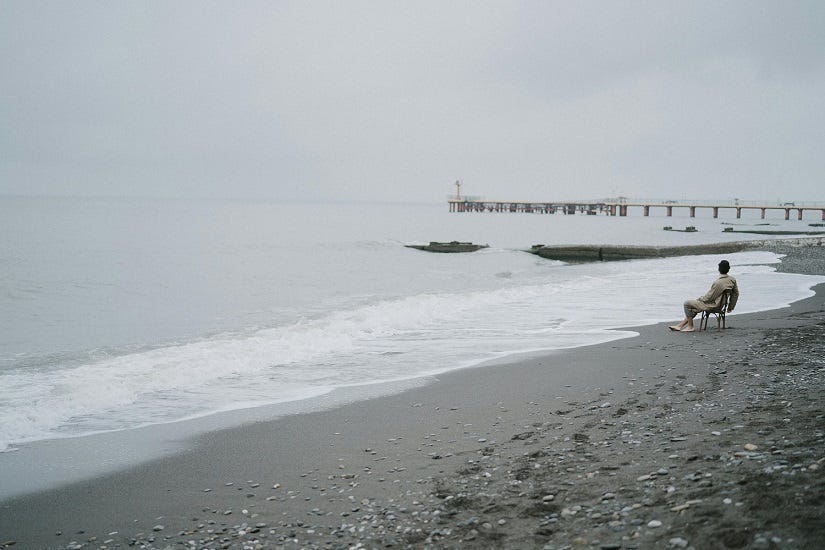 A calm sea and a man sitting on a chair near it.