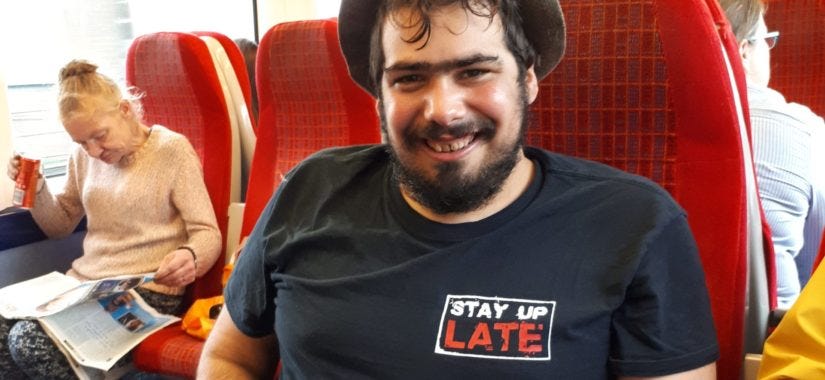 Smiling man sitting on a train wearing a Stay Up Late t-shirt