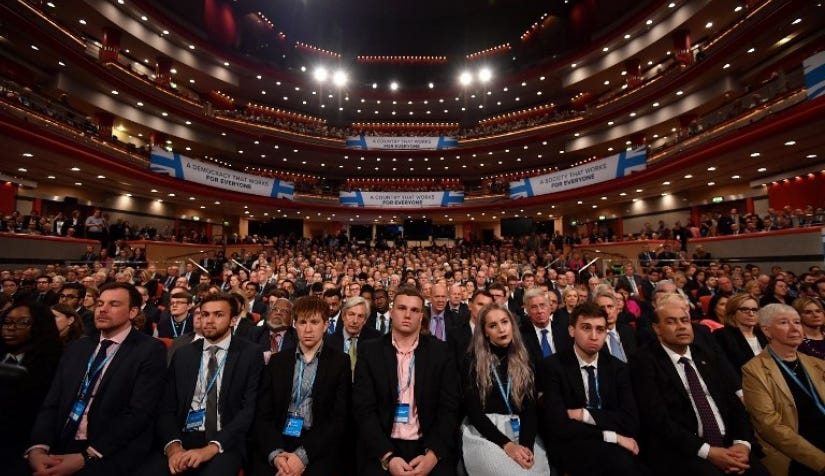 A photograph of the attendees at the UK Conservative Party Conference, 2022. They’re all wearing suits, nearly all white, mostly men and all looking bored.