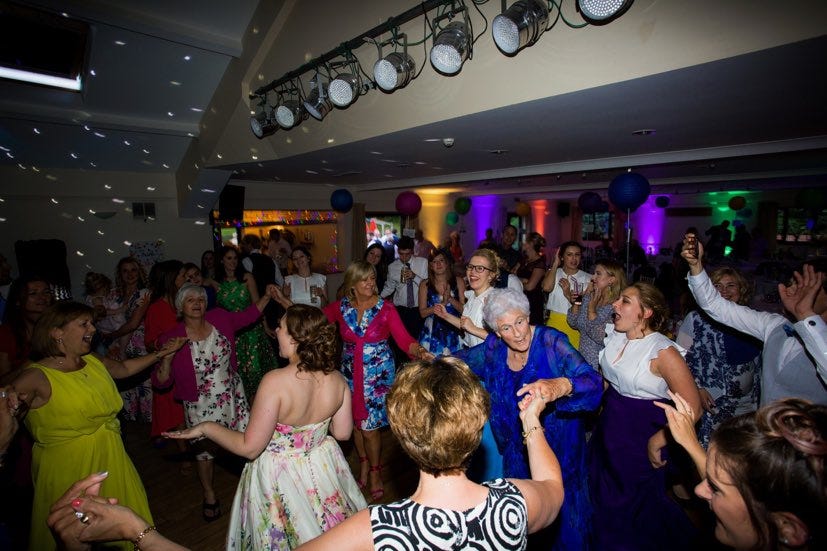 Granny in a signiture blue dress dancing at a wedding surrounded by a lot of people