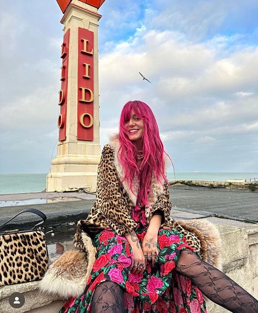 Florence Given sitting by seaside in colourful outfit.