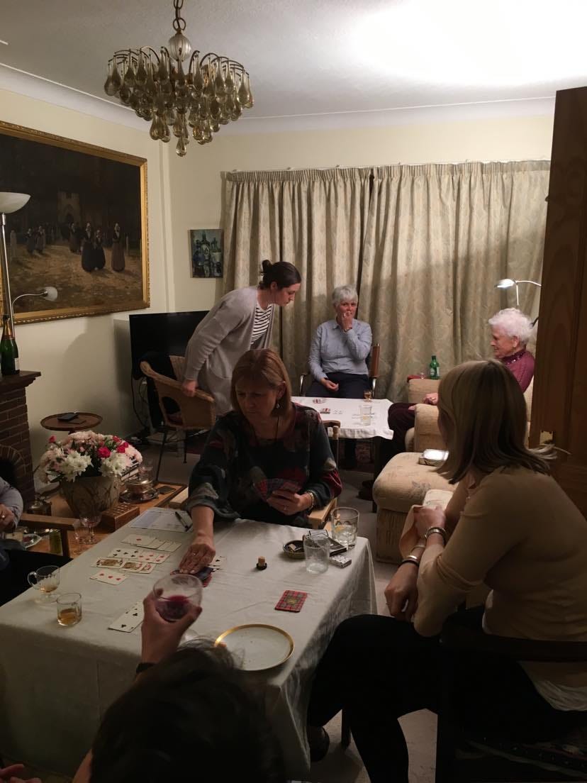 8 people sat around two card tables in a living room playing cards