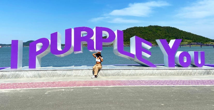 A sign that says ‘I Purple You’ that my friend is posing in front of.