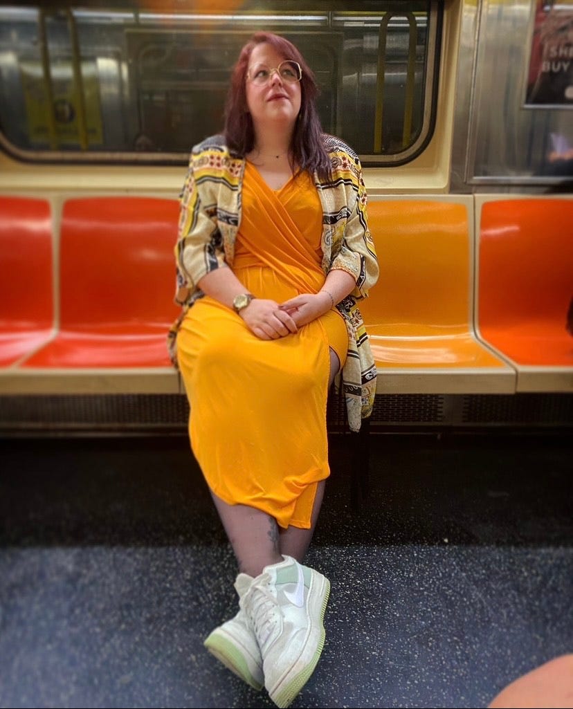 A photo of Bella on the subway in NYC, wearing an orange dress sitting on orange seats. She is a 34 year old white woman, most accurately described as a “small fat”