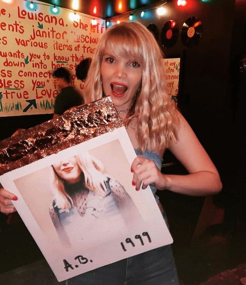 A girl with long blonde hair and a blue shirt holds a sign in a bar