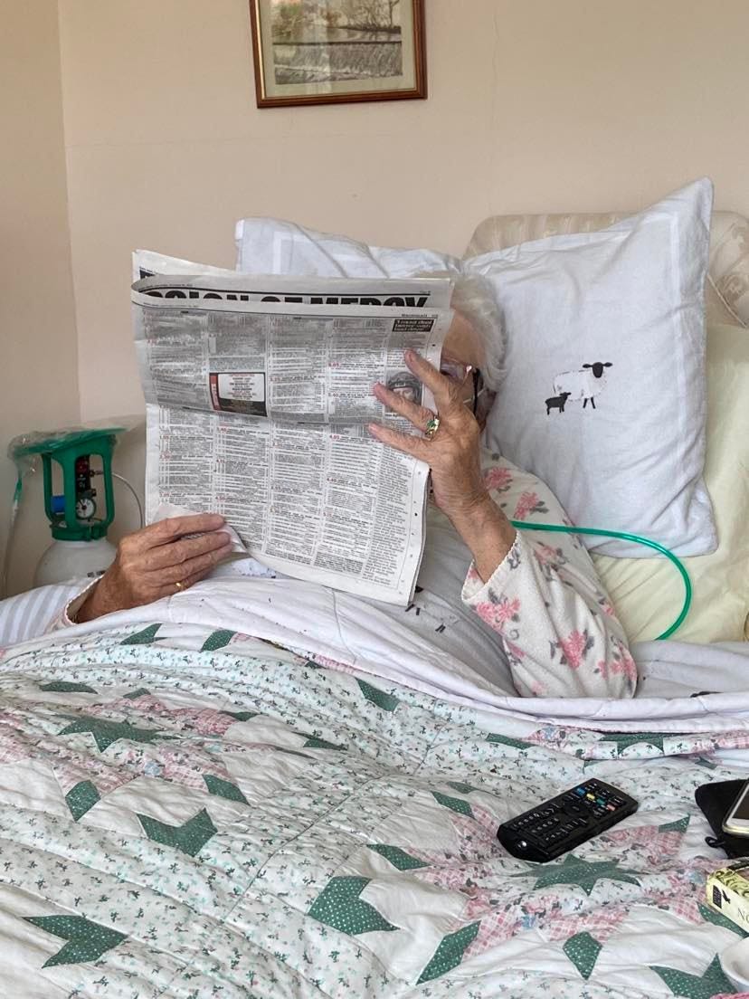 Granny in bed behind a paper looking a the horses