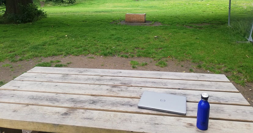 A closed laptop and a water bottle on a picnic bench in a park