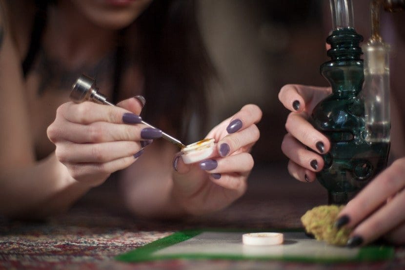 Women with painted fingernails setting scooping concentrates and holding a dab rig.