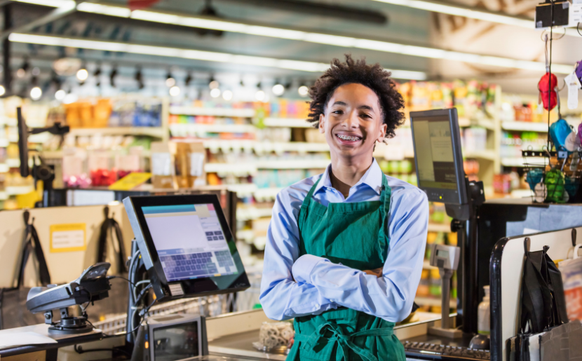 A student poses for a photo behind a supermarket cash register.