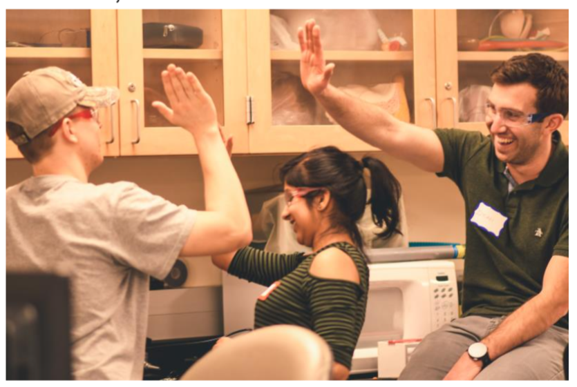 3 people high five in front of a workbench