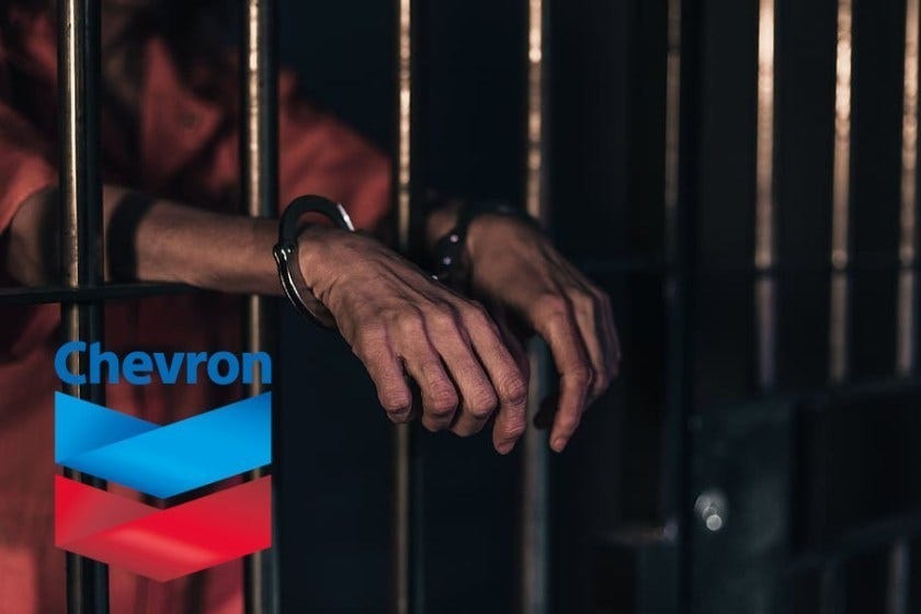 A pair of handcuffed hands sticking between prison bars, with the Chevron logo in the bottom left corner.