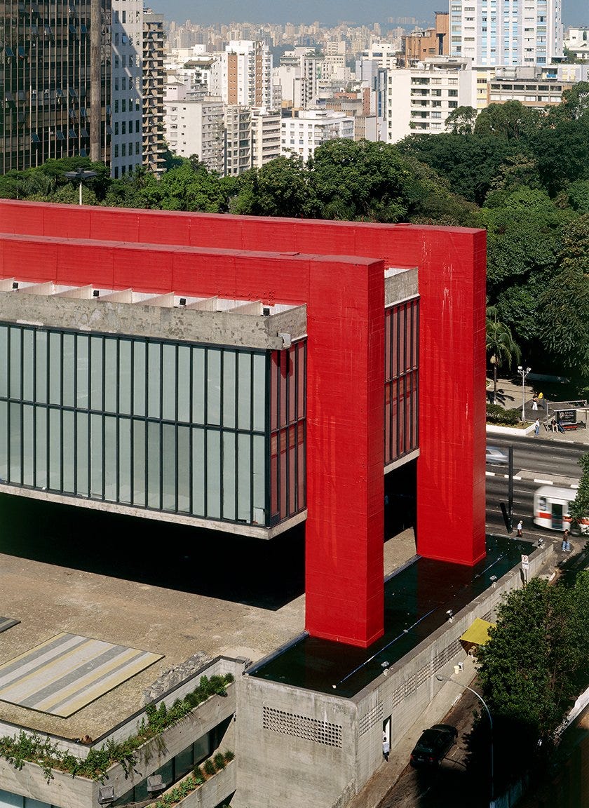 The museum hovers off the ground, supported by two massive bright red beams. The monolithic columns terminate in a reflecting