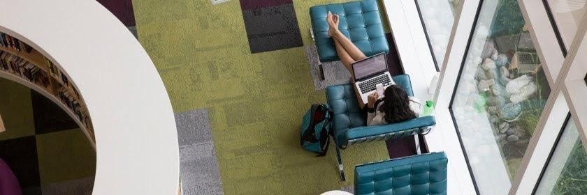 A young women sitting in study hall on her phone and labtop.