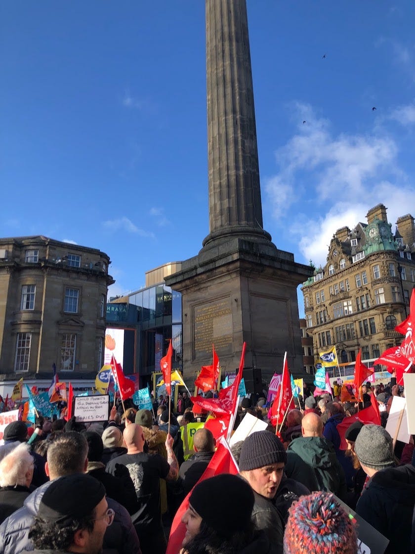 A large group of protestors gather outside waving red flags.