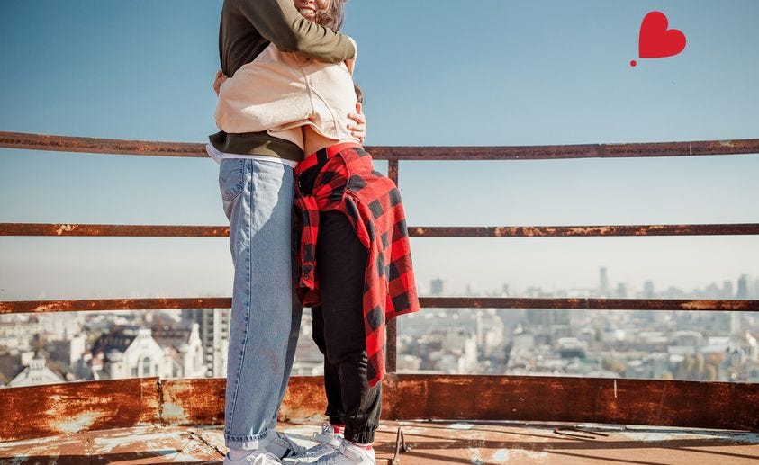A couple standing on a rooftop, forming a heart shape with their arms, representing love and romance.