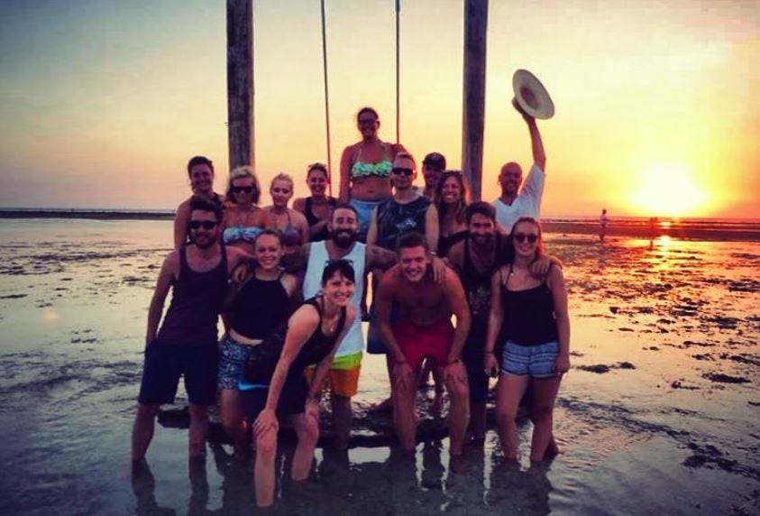 Alex Innes in Bali with a group of friends, on the beach with sunset in the background