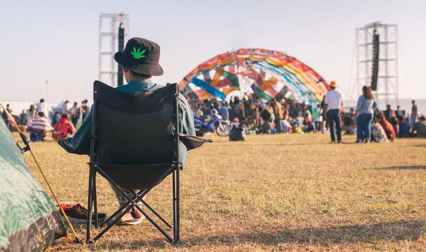 A man in a chair wearing a cannabis hat at a cannabis festival.