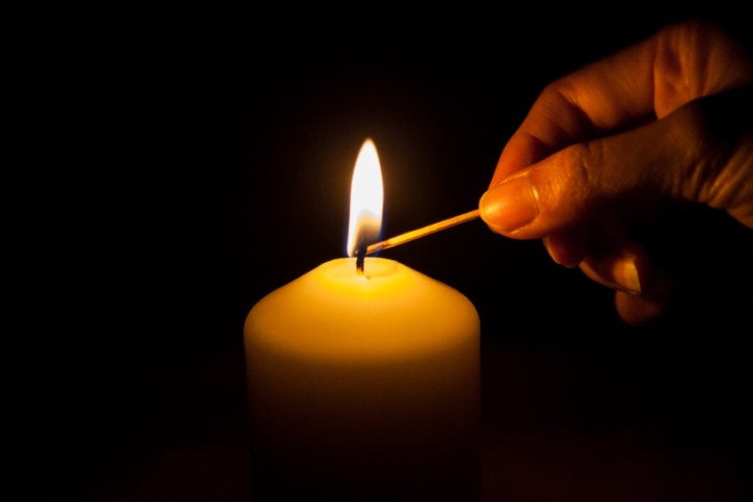 a hand lighting a beeswax candle in a dark setting