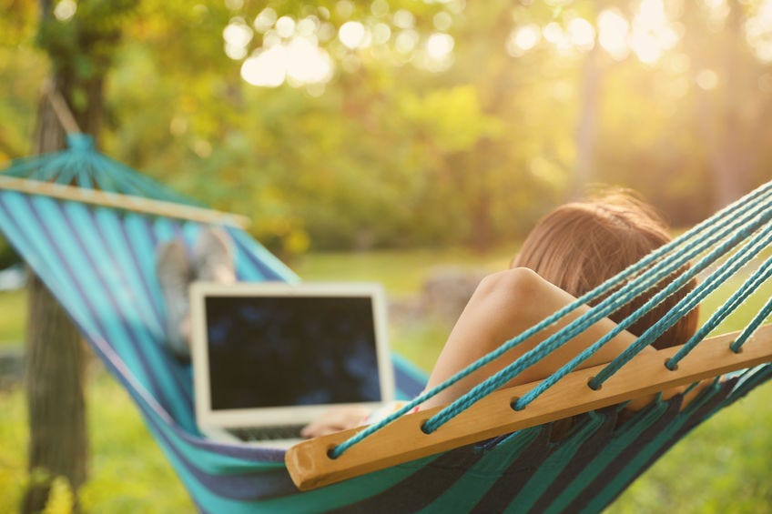 a person lying in a hammock in a wooded area using a laptop