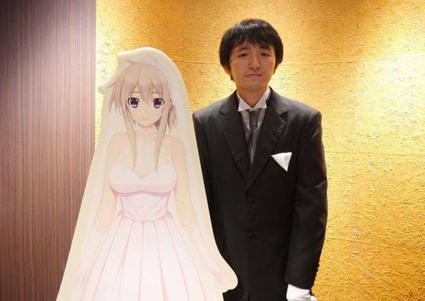 A Japanese man poses next to a bust of the anime character he married.