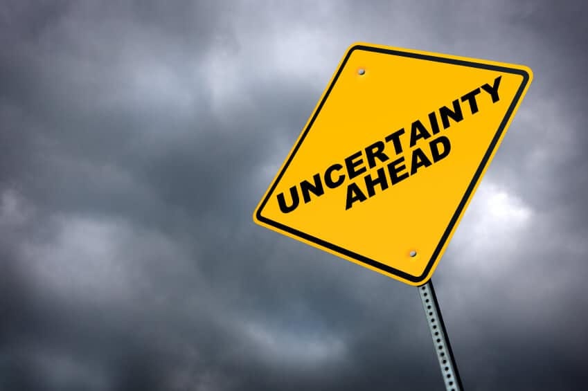 Dark and cloudy sky with a yellow sign mentioning "uncertainty ahead"