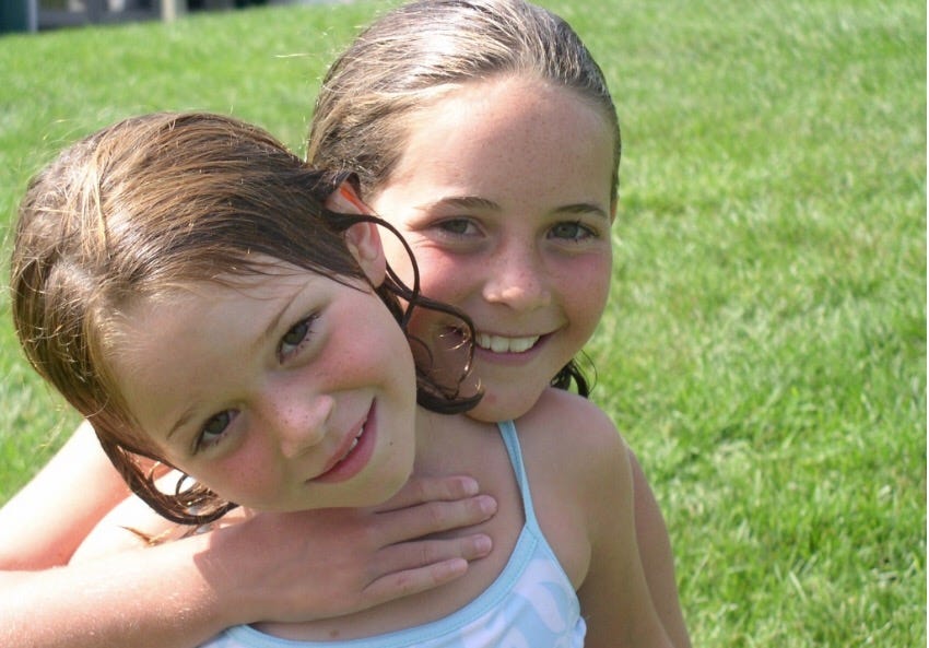 Two young girls embracing in a grassy field.