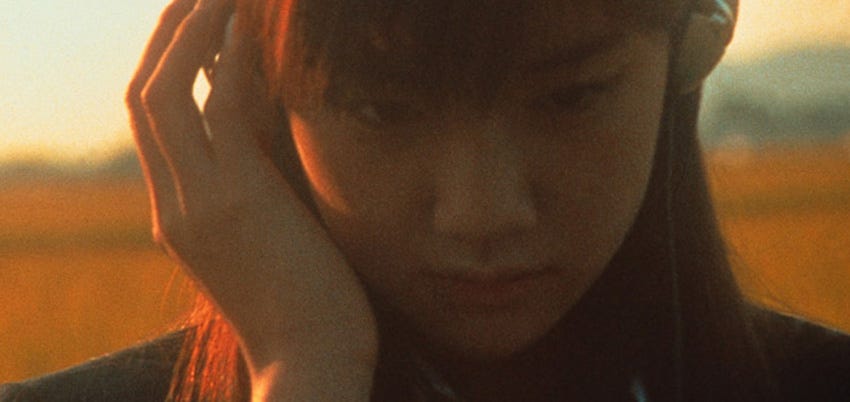 An upclose shot of a teen girl with a pondering yet melancholic expression, she’s listening to music with headphones and is using her left hand to press the leftside of the headphone closer to her ear. The shot is taken during sunset hour, giving the quality of the shot a rich golden glow.