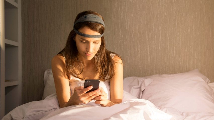 A woman wears the DREEM 3 headband in bed, while scrolling through her phone.