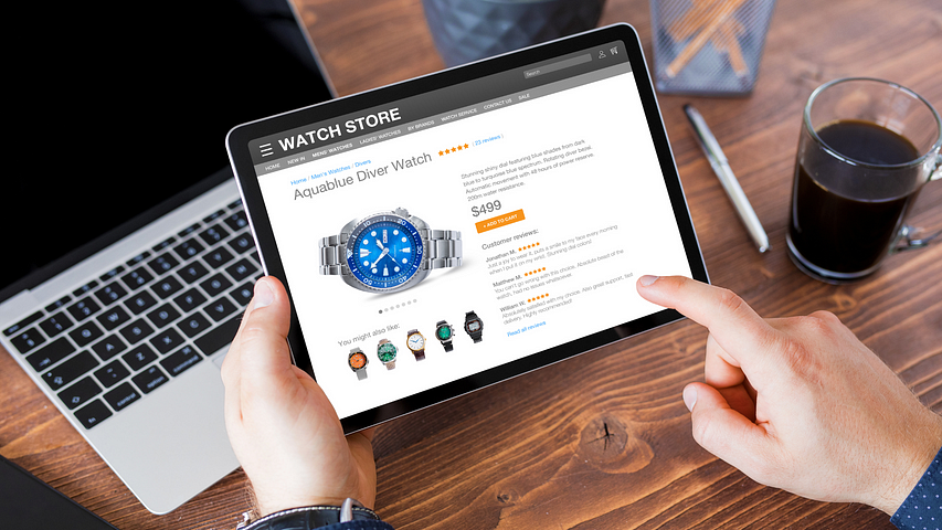 Man holding a tablet, contemplating a $500 purchase on an aqua blue diver watch from an online watch store displayed on his computer, embodying the decision-making process in high-end ecommerce, as explored in our article on selling expensive Amazon products.