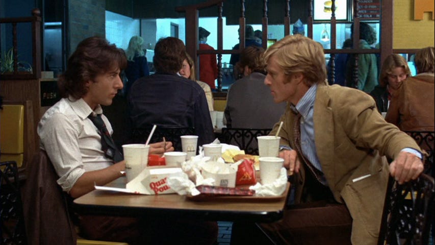 Still from the movie All the President’s Men. Two men looking at each other across a table in a fast food restaurant.