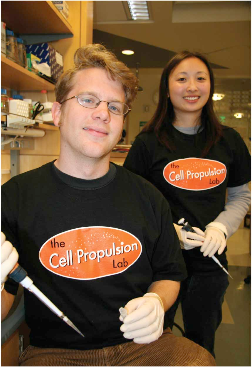 Photograph of Angi standing behind a smiling person wearing glasses. They are both wearing T-shirts that say “the cell propulsion lab.”