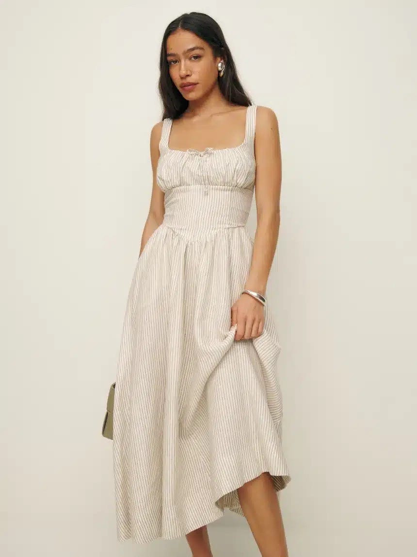 Model wearing a cream colored, midi length, milkmaid style sundress.