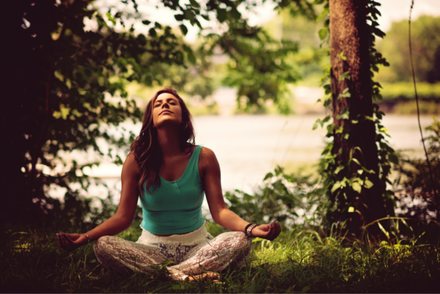 Woman sits to meditate in nature near trees and water