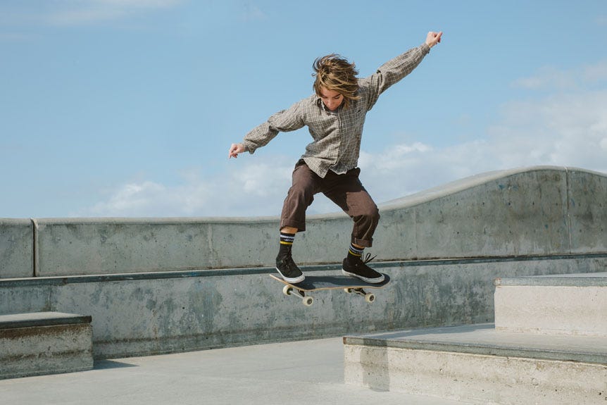 Young woman jumping skateboard off ledge in concrete skatepark
