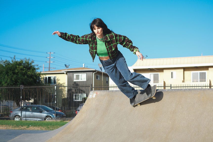 Young woman skateboarding on low concrete ramp inside skatepark