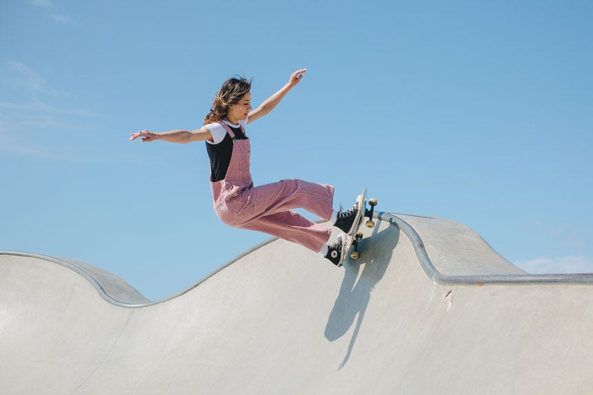 Young woman riding skateboard on two wheels in concrete skatepark bowl