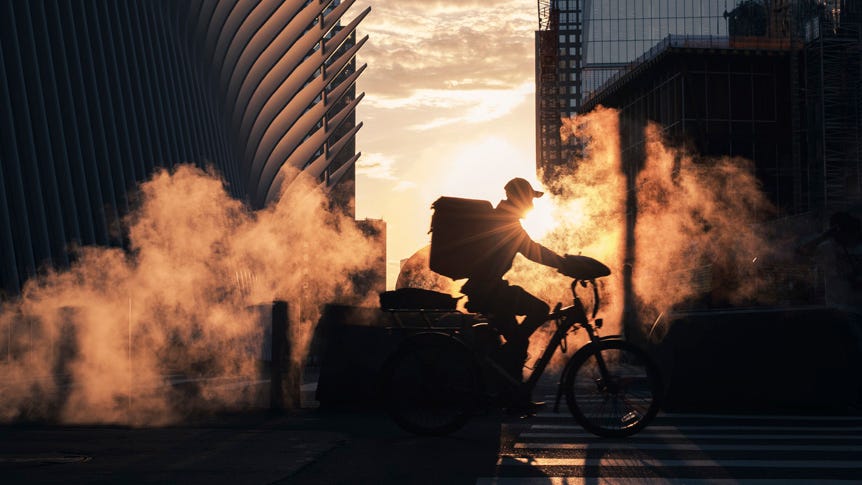 Silhouette of man cycling through steam on New York street during sunrise