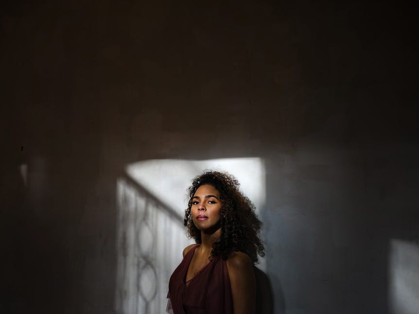 Model standing in shaft of window light, surrounded by shadows