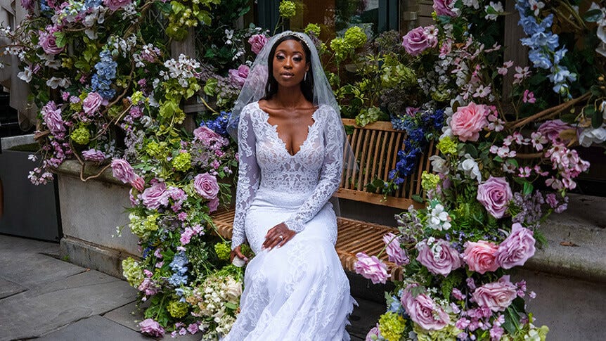 Young, African-American bride sitting on bench surrounded by flowers